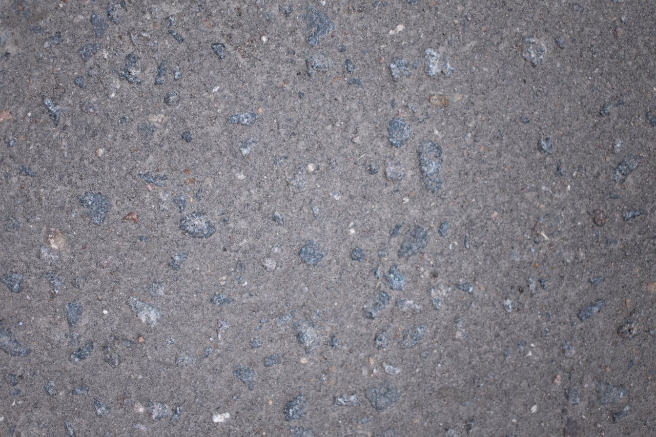 Top view of gray rough textured asphalt with stone inclusions scattered on surface